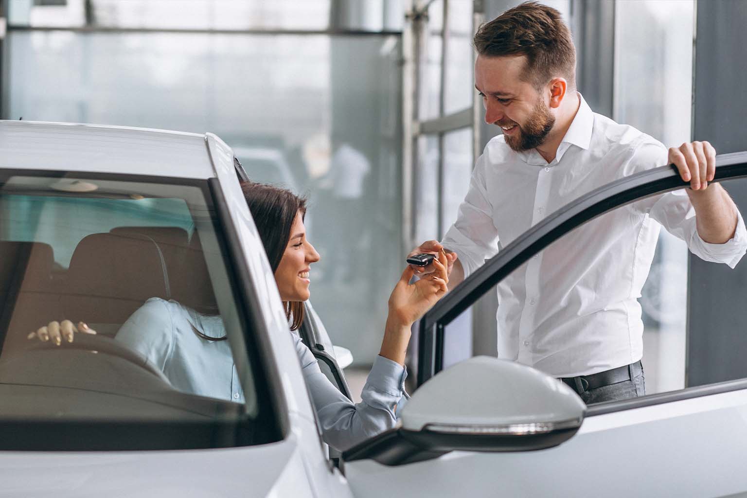 Vendedor entrega chaves de carro branco para cliente sorridente, simbolizando a conquista de patrimônio com o Crédito em Dobro Lyscar Consórcios.
